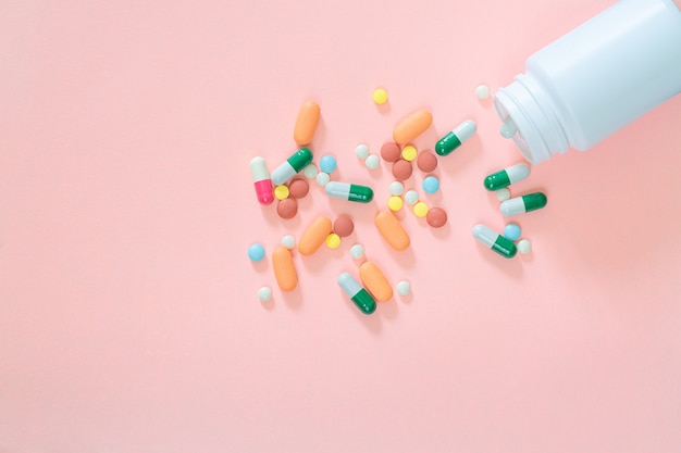 Разноцветные таблетки таблетки капсулы в пластиковой бутылке на розовом фоне копией пространства