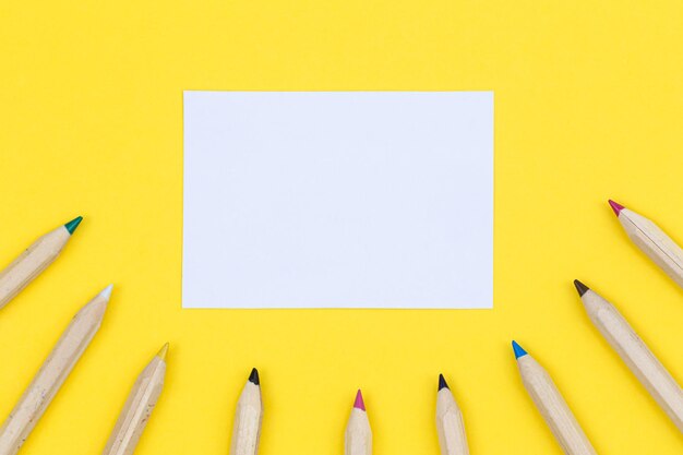 Free photo multicolored wooden pencils and piece of paper on a yellow background