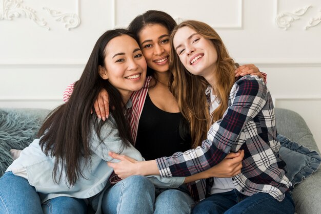 Multiethnic best girlfriends hugging and sitting on sofa