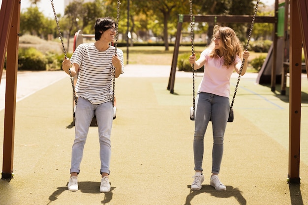 Free photo multiethnic couple of teenagers swinging on playground