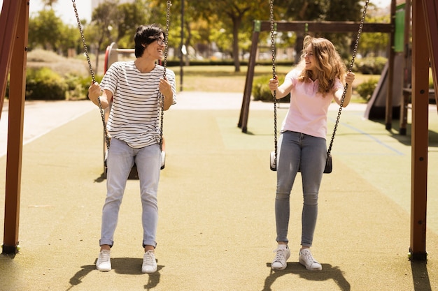 Multiethnic couple of teenagers swinging on playground