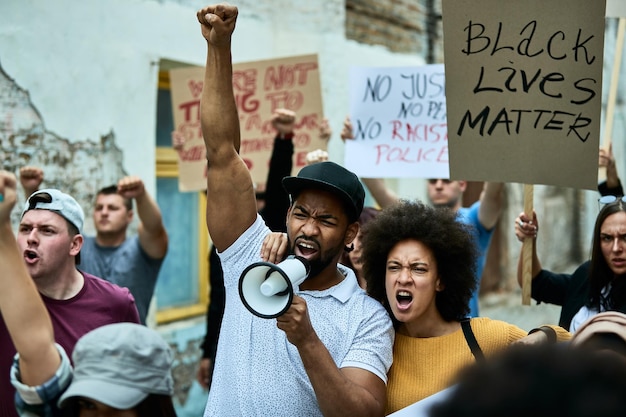 Multiethnic crowd of people fighting for freedom on a protest against racial discrimination Focus is on African American couple shouting through megaphone