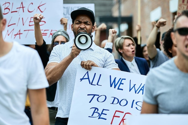 Folla multietnica di persone che protestano contro il razzismo nelle strade della città il focus è sull'uomo afroamericano che grida attraverso il megafono