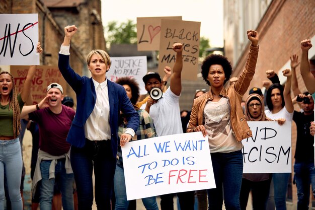 Multiethnic crowd of people with raised fists protesting for human rights while carrying antiracism placards through city streets