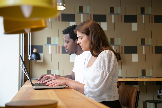 Multiethnic designers sitting together and working on laptops in coworking space