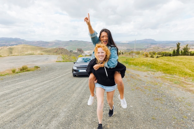 Multiethnic females playing piggyback on roadside