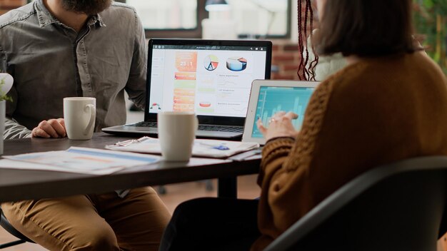 Multiethnic group of colleagues working on charts analysis with digital tablet, using online research information to create infographics report. People analyzing diagrams in boardroom.