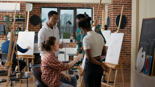 鉛筆と帆布を使用して個人の成長のための花瓶モデルを作成し、アートクラスで一緒にスケッチを描くことを学ぶ学生の多民族グループ。描画スキル開発のためのワークショップ。