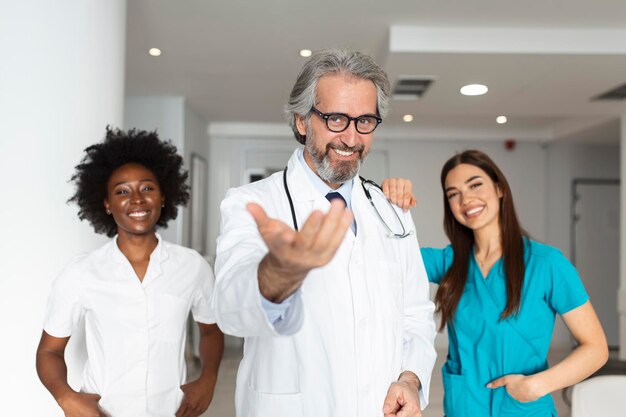 Free photo a multiethnic group of three doctors and nurses standing in a hospital corridor wearing scrubs and coats the team of healthcare workers are staring at the camera and smiling