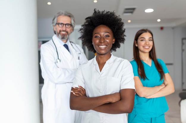 Free photo a multiethnic group of three doctors and nurses standing in a hospital corridor wearing scrubs and coats the team of healthcare workers are staring at the camera and smiling