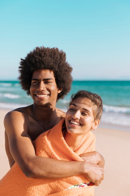 Multiethnic smiling couple on beach hugging  