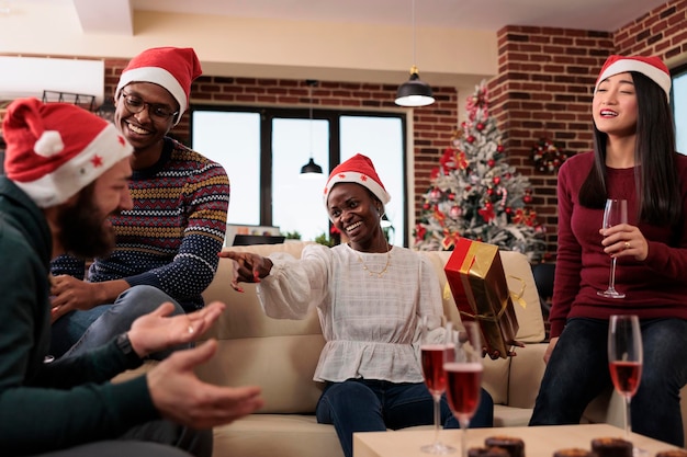 Multiethnic team of colleagues exchanging gifts at christmas office party, celebrating xmas festivity with alcohol and presents. Having fun with surprise at holiday celebration.