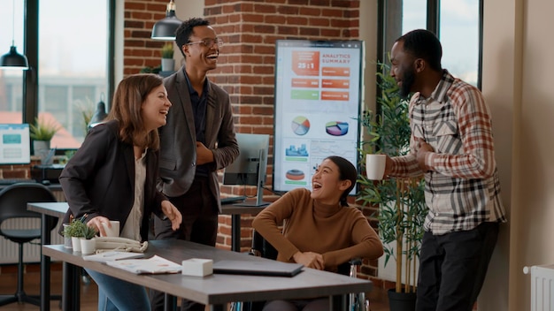 휴식 시간에 만나 비즈니스 협업에 대해 토론하는 다민족 직원 팀. 행복한 사람들은 웃고 사무실에서 마케팅 프로젝트를 계획합니다. 핸드헬드 샷.