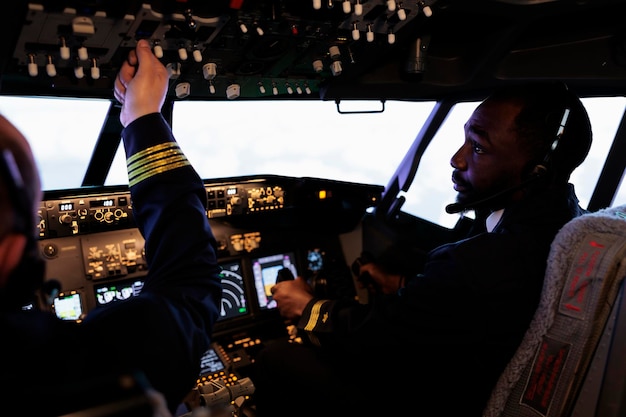 無料写真 コックピットのコントロール パネルを使用して飛行機を飛ばし、電源スイッチとダッシュボードのコマンド ボタンを押して離陸する多民族のパイロット チーム。機内に乗組員がいる国際航空サービス。