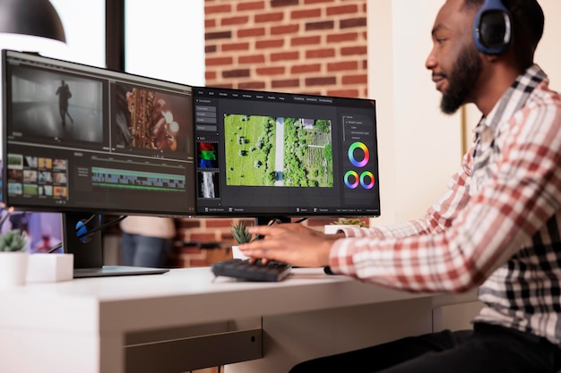 Editor multimediale che utilizza un software per modificare le riprese video su più monitor a casa, modificando i filmati con l'applicazione di produzione sul computer. lavorare al montaggio di film per creare contenuti multimediali.