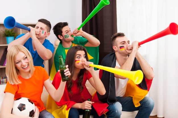 Multinational friends blowing by vuvuzela during the football match