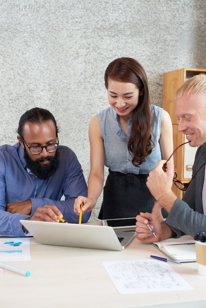 Multinational group of colleagues looking at laptop screen at work meeting in office