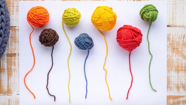 Multiple colored partially unwounded balls of yarn on a white paper. Top view