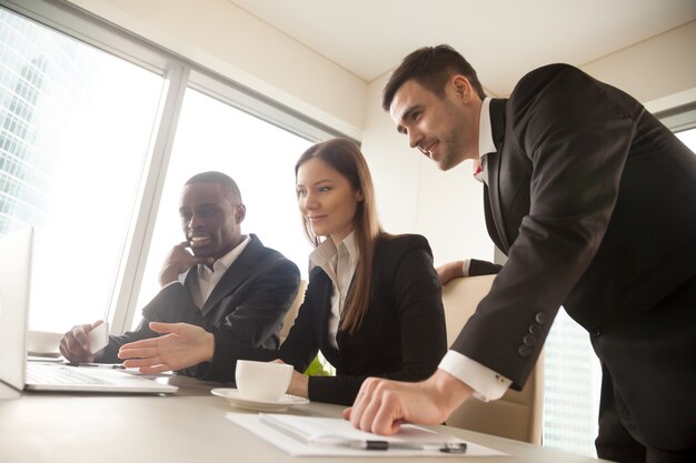 Multiracial business partners using laptop during meeting, looki