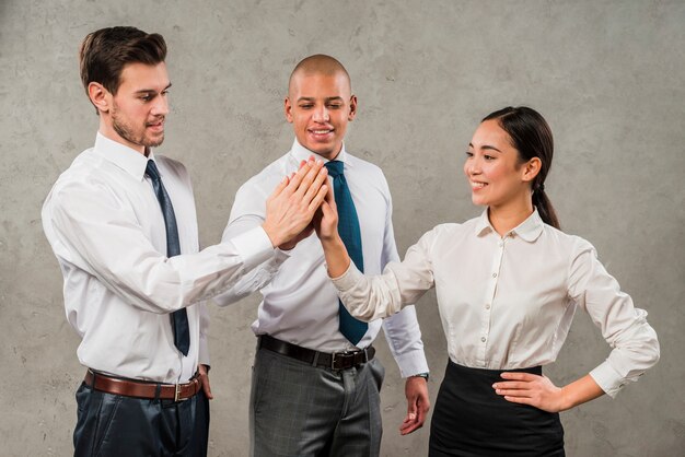 Multiracial businesspeople giving high-five to each other in front of grey wall