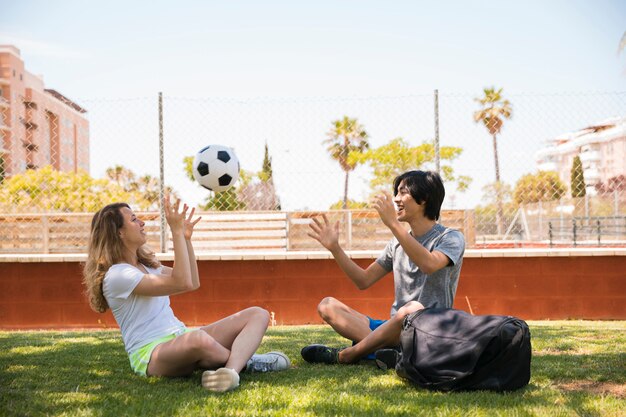 Multiracial couple throwing soccer ball while sitting on grass