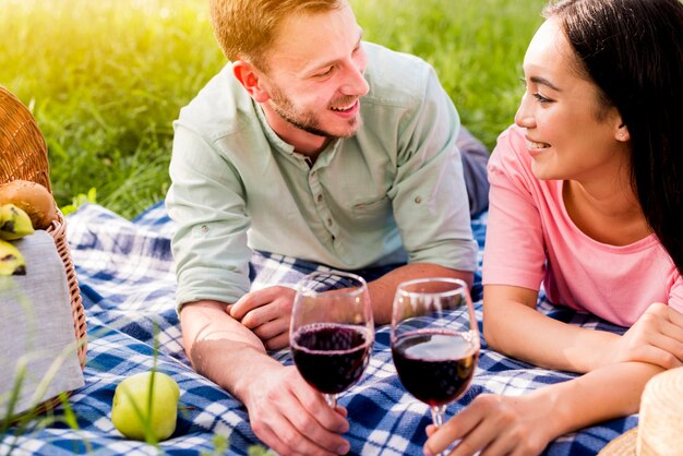 ピクニックに市松模様の格子縞の上に横たわる多民族の笑みを浮かべて夢中のカップル