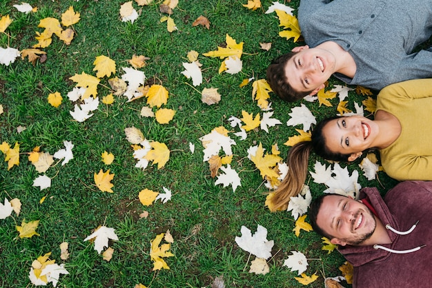 Multiracial young friends lying on grass with autumn leaves