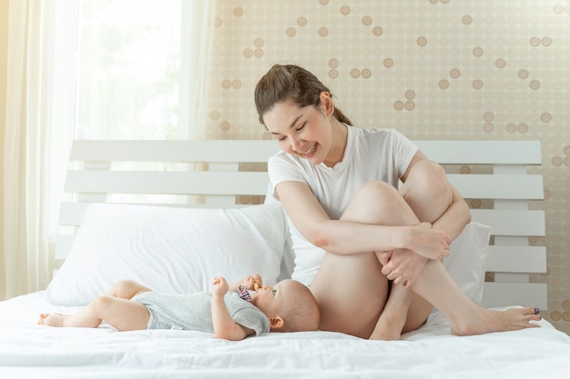 Mum and baby happily tease each other on a white bed.