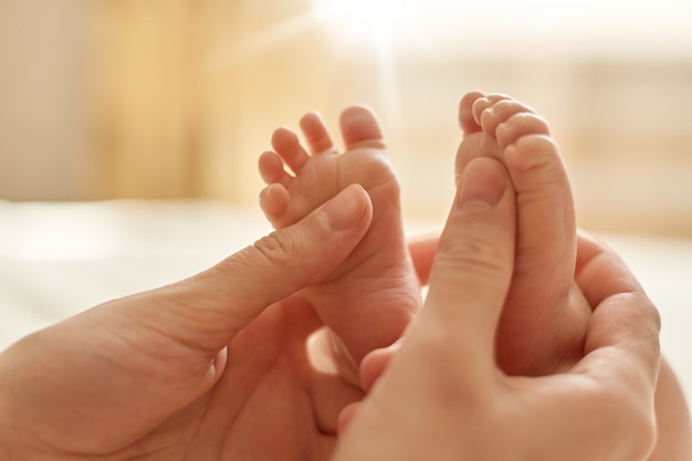 赤ちゃんのマッサージをするお母さん、乳児の素足をマッサージするお母さん、新生児の予防マッサージ、明るい背景に両手で赤ちゃんの足をなでるお母さん。