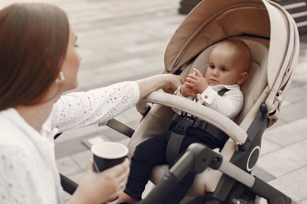 Mum sitting on a bench. Woman pushing her toddler sitting in a pram. Family concept.