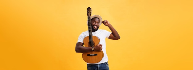 Free photo muscular black man playing guitar wearing jeans and white tanktop isolate over yellow background