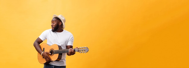 Free photo muscular black man playing guitar wearing jeans and white tanktop isolate over yellow background