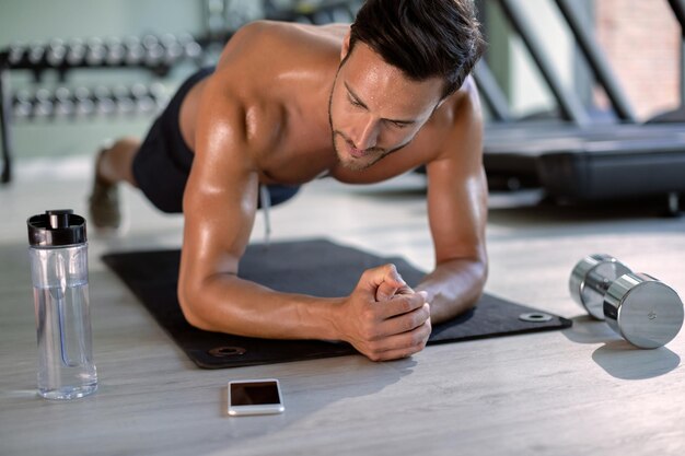 Muscular build athlete exercising in plank pose during cross training at health club