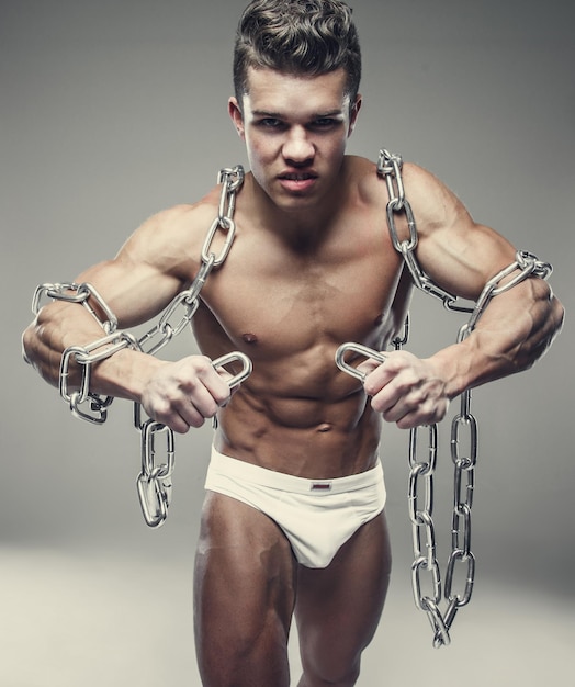 Muscular female model in white panties posing with silver chain in a studio.