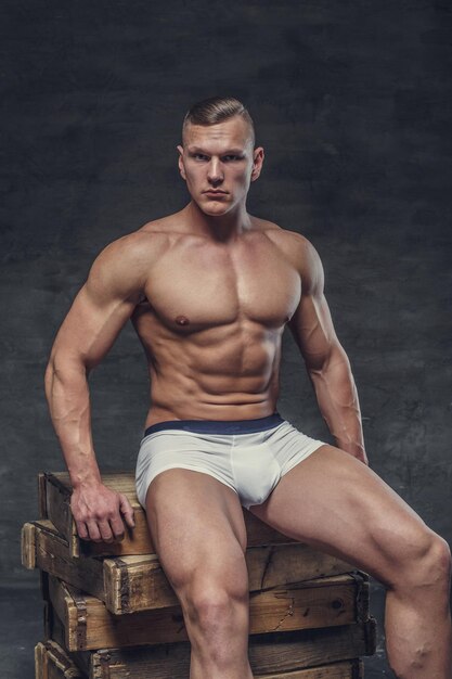 白いパンティーの筋肉の男は木箱に座っています。