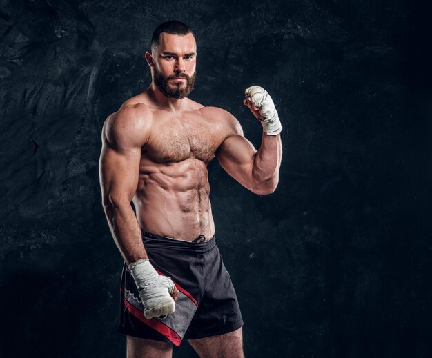 Muscular handsome fighter with naked torso is demonstraiting his power at dark photo studio.