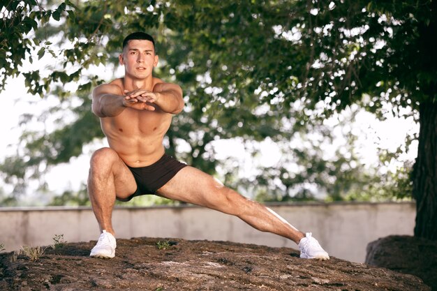 A muscular male athlete doing workout at the park. Gymnastics, training, fitness workout flexibility.