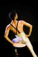 Foto gratuita ballerino di balletto maschio muscolare che si siede sotto i riflettori
