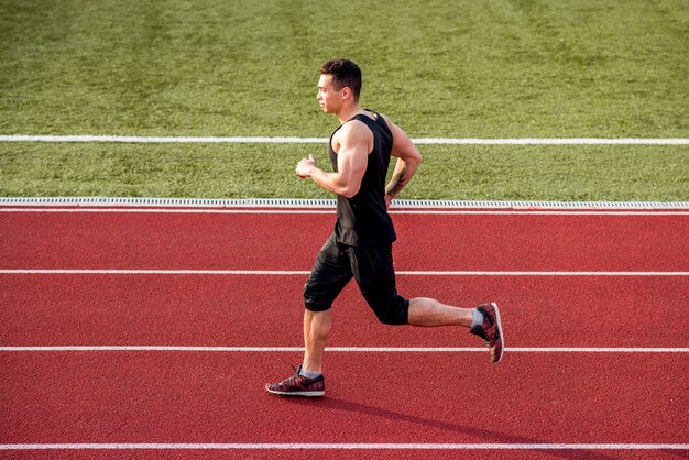 Muscular male runner running on red race track