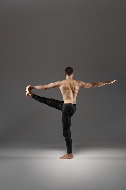 Muscular male yoga doing stretching exercise on grey background. strong man practicing yogi   asana training  top concentration  healthy lifestyle