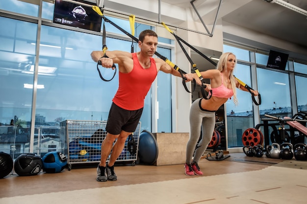 체육관에서 익스팬더로 운동을 하는 근육질의 남자와 운동하는 여자.