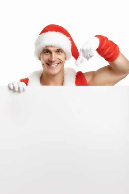 Мышечное человек, переодетый Санта-Клауса, указывая на пустой рекламный щит, улыбаясь