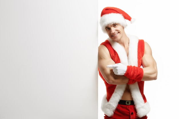 Muscular man disguised as santa leaning against a white sign