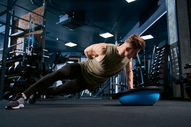 Muscular man doing push ups on one hand.