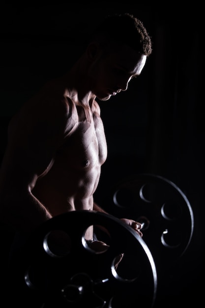 Muscular man doing weightlifting in fitness center