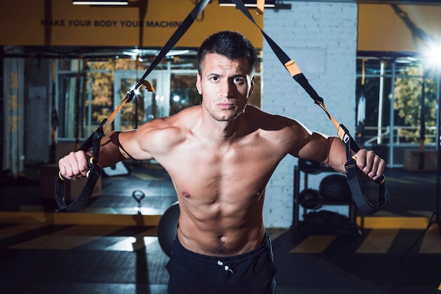 Muscular man exercising with fitness strap in gym