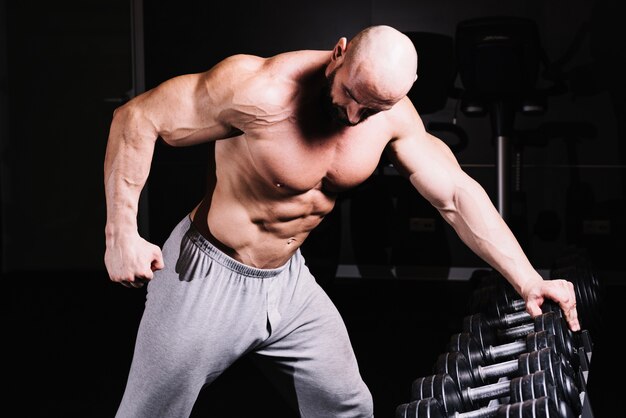 Muscular man leaning on dumbbell rack