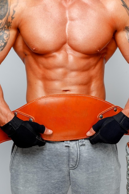 Free photo muscular man poses showing his body and holding power belt