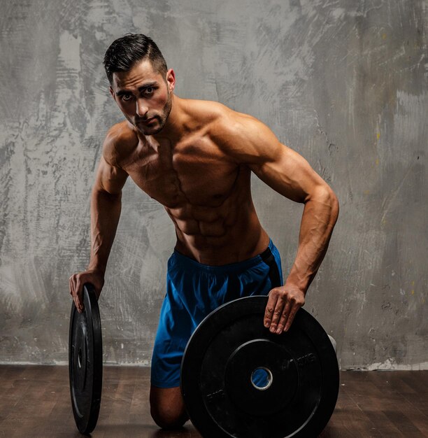 Muscular man with naked torso holding weights. Grey background