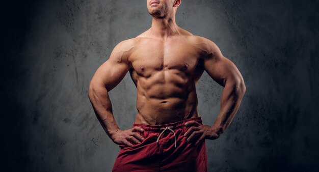 Muscular man with nice muscules is posing for photographer at dark photo studio.